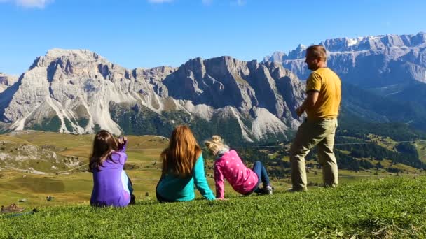 Родители и дети сидят на траве и смотрят на горы — стоковое видео