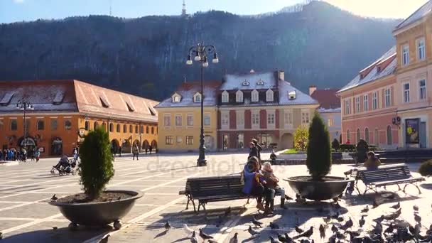 Niños alimentando palomas en una plaza principal de la ciudad rumana Brasov — Vídeos de Stock