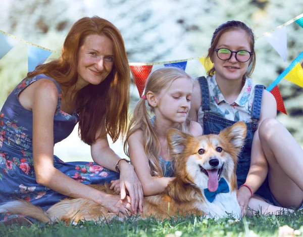 Madre con sus hijas y perro están sentados en una hierba — Foto de Stock