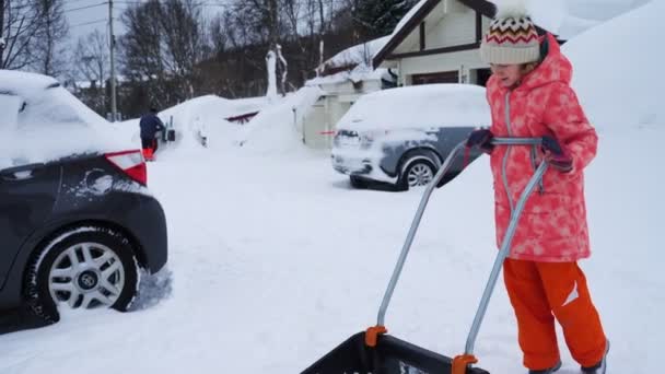 冬の吹雪の後にシャベルで雪の道をきれいにするのを手伝っている子供の女の子 — ストック動画