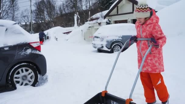 冬の吹雪の後にシャベルで雪の道をきれいにするのを手伝っている子供の女の子 — ストック動画