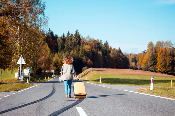 幸せな旅だ少女はバラの側面に黄色のスーツケースを持った仕切りの帯に沿って行き — ストック写真