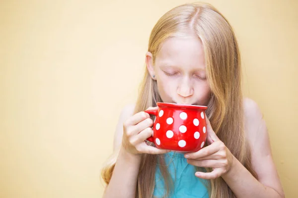 幸せな笑顔の女の子は大きな赤いカップからミルクを飲む 夏と井戸 — ストック写真
