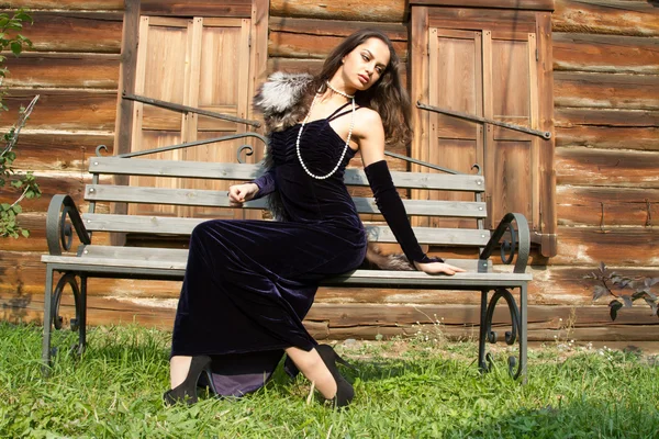 Young girl in an evening dress on a background of the old wooden houses with shutters closed — Stock Photo, Image