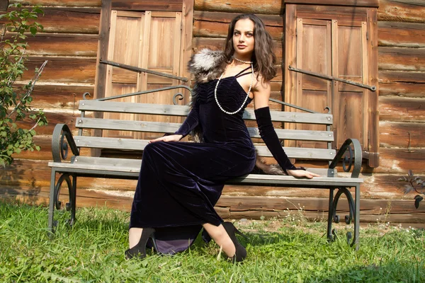 Young girl in an evening dress on a background of the old wooden houses with shutters closed — Stock Photo, Image