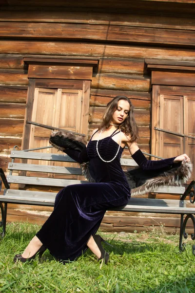 Junges Mädchen im Abendkleid vor dem Hintergrund der alten Holzhäuser mit geschlossenen Fensterläden — Stockfoto