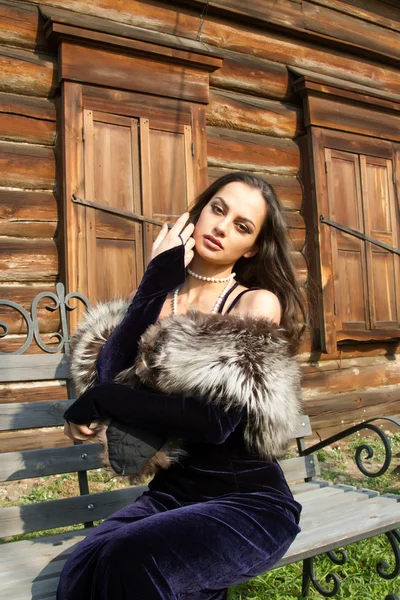 Young girl in an evening dress on a background of the old wooden houses with shutters closed — Stock Photo, Image