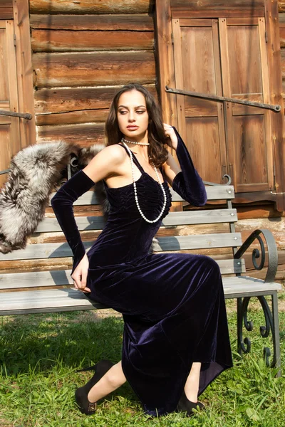 Chica joven en un vestido de noche sobre un fondo de una vieja casa de madera — Foto de Stock