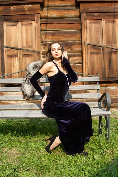 Menina jovem em um vestido de noite em um fundo de uma velha casa de madeira — Fotografia de Stock