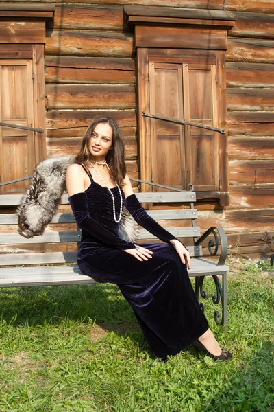 Young girl in an evening dress on a background of an old wooden house — Stock Photo, Image