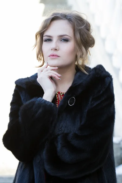 Beautiful young girl in a black fur coat — Stock Photo, Image