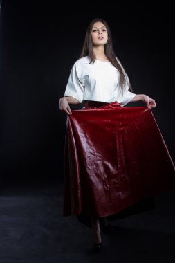 Güzel genç kız beyaz bir bluz ve siyah bir zemin üzerine uzun etek kırmızı. Stüdyo portre.