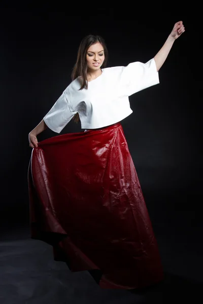 Beautiful young girl in a white blouse and a long skirt red on a black background. Studio portrait. — Stock Photo, Image