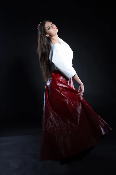 Beautiful young girl in a white blouse and a long skirt red on a black background. Studio portrait. — Stock Photo, Image