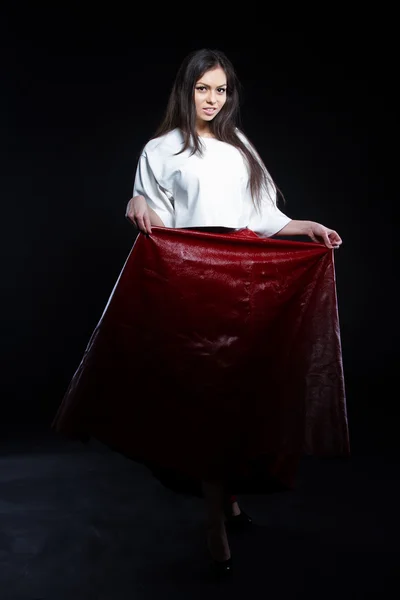 美丽的年轻女孩，在一件白色衬衫和黑色背景上的长裙子红。工作室画像. — 图库照片