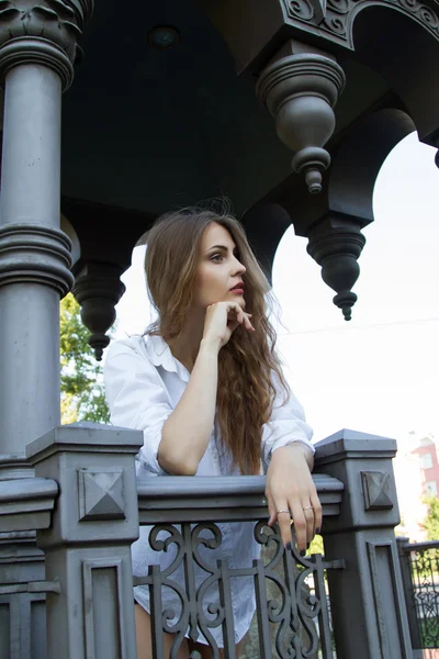 Menina em uma camisa branca de pé em um gazebo de metal — Fotografia de Stock