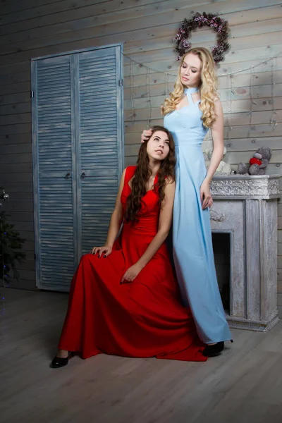 Twee jonge meisjes in lange jassen in een kamer met een open haard — Stockfoto
