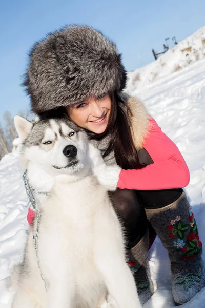 Chica con Husky perro crianza en un fondo de nieve cubierto de bosque — Foto de Stock