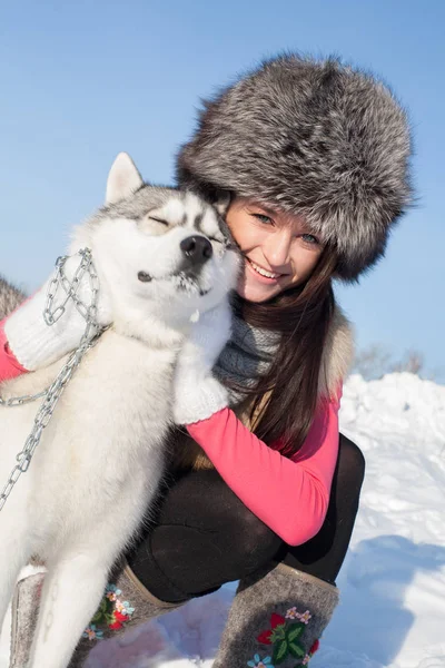 Chica con Husky perro crianza en un fondo de nieve cubierto de bosque —  Fotos de Stock