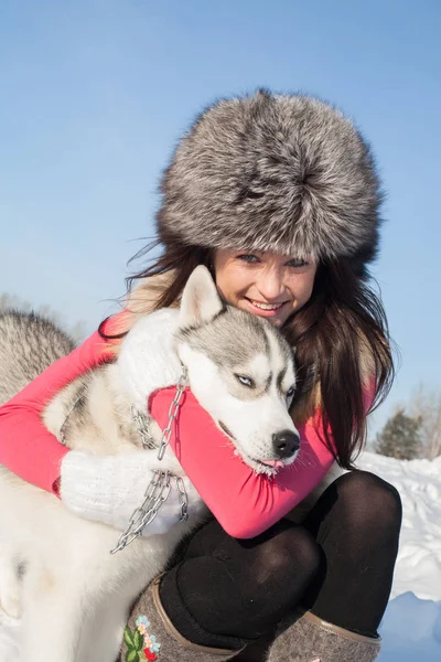 Chica con Husky perro crianza en un fondo de nieve cubierto de bosque —  Fotos de Stock