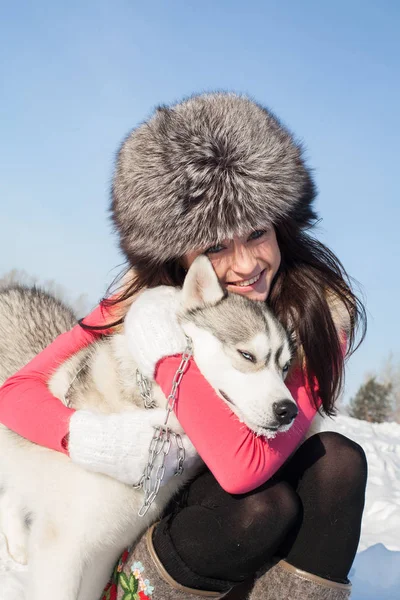 Chica con Husky perro crianza en un fondo de nieve cubierto de bosque — Foto de Stock