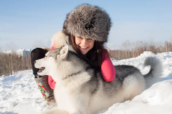 Chica con Husky perro crianza en un fondo de nieve cubierto de bosque —  Fotos de Stock