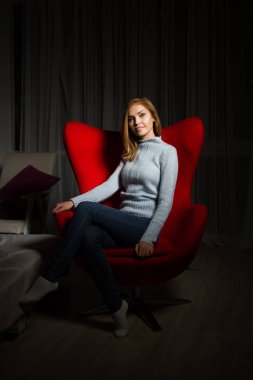 sarışın karanlık bir odada kırmızı bir sandalyede oturur