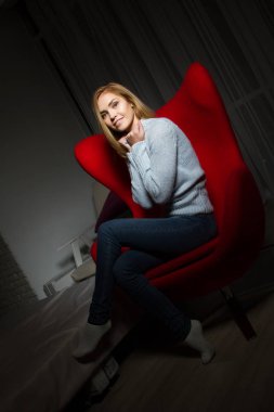 sarışın karanlık bir odada kırmızı bir sandalyede oturur