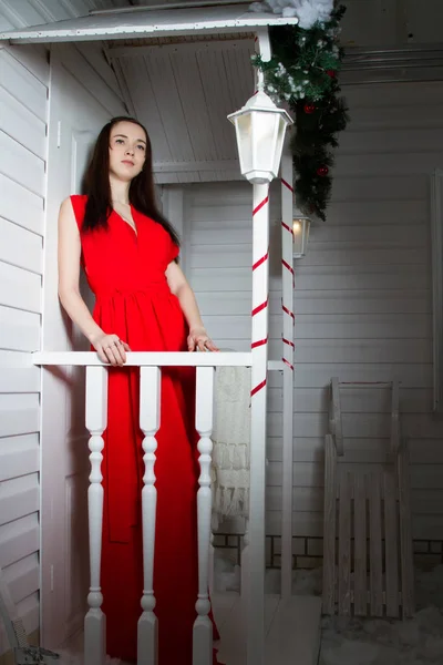 Дівчина в червоній вечірній сукні, що стоїть на ганку будинку . — стокове фото