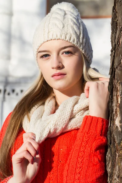Girl in a knitted cap and mittens standing, leaning against a tree — Stock Photo, Image