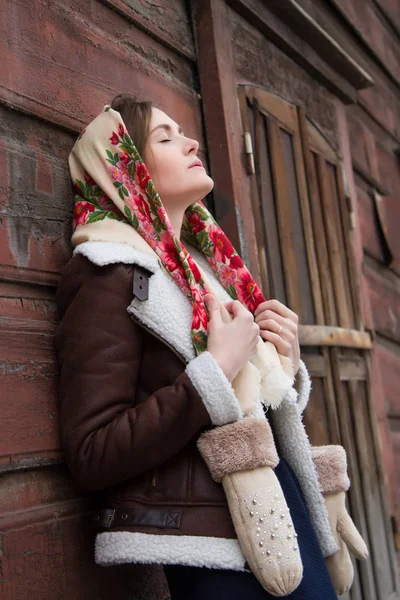 Girl in a scarf on the background of an old wooden house — Stock Photo, Image