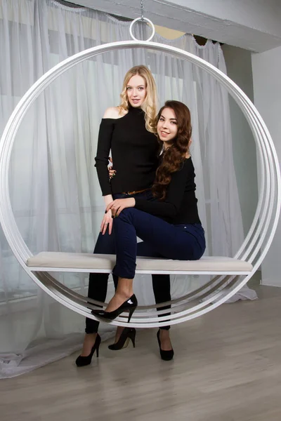 Dvě dívky v džíny sedí na houpačce — Stock fotografie