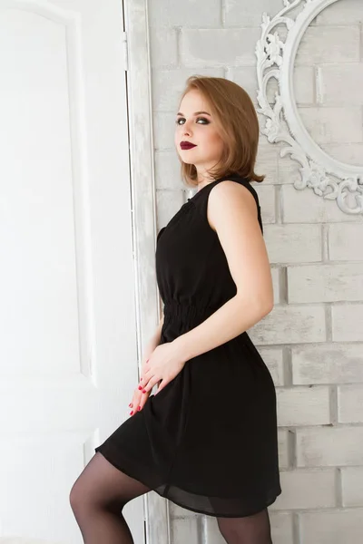 Girl in a short black dress standing leaning against the brick wall — Stock Photo, Image