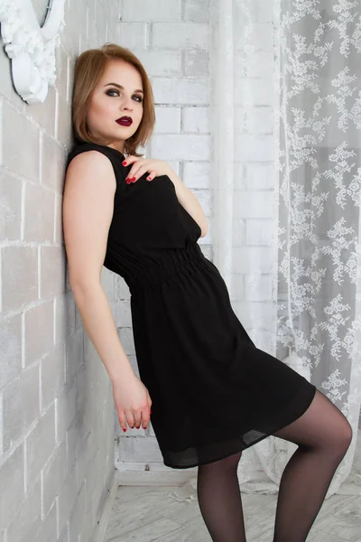 Девушка в коротком черном платье стоит, прислонившись к кирпичной стене — стоковое фото