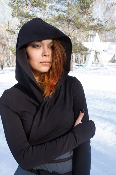 Flicka i huven på bakgrunden av snötäckta park — Stockfoto