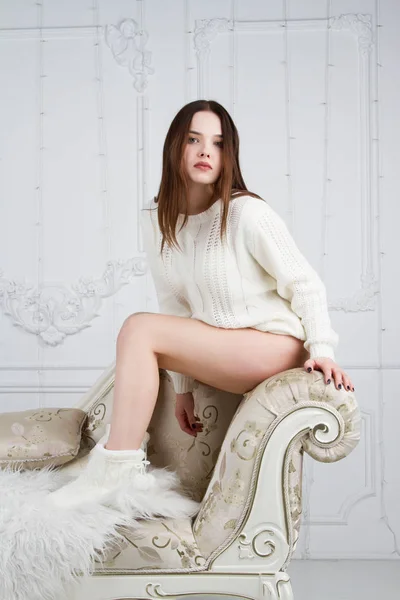 Dziewczyna w biały sweter, siedząc na kanapie tapicerowane z światła — Zdjęcie stockowe