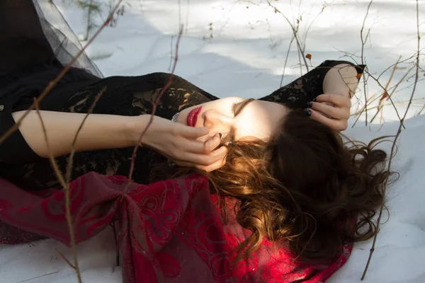 Ung flicka liggande i snön i vinter skogen — Stockfoto