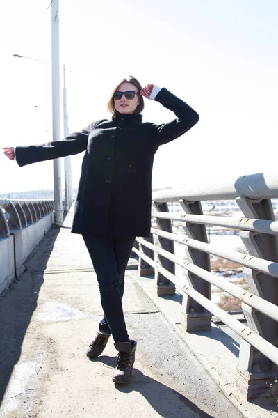 Jeune fille dans un manteau et jeans est debout sur un pont — Photo