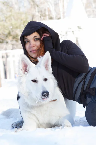 Flicka med en vit hund ligger på snön — Stockfoto