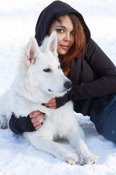 Κορίτσι με ένα λευκό σκυλί βρίσκεται στο χιόνι — Φωτογραφία Αρχείου