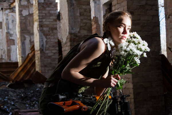 Девушка-снайпер на развалинах с букетом цветов
