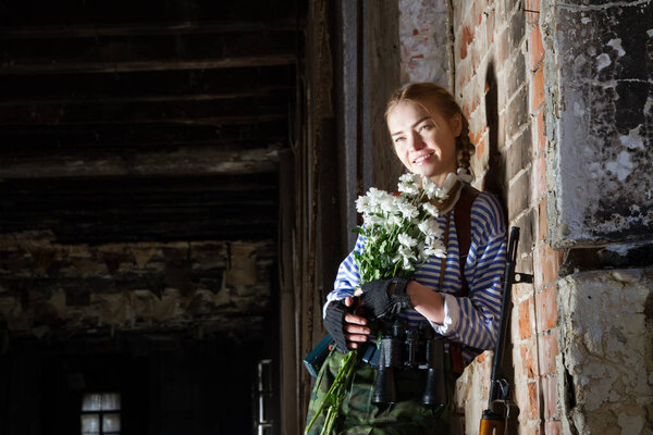 Девушка-снайпер на развалинах с букетом цветов
