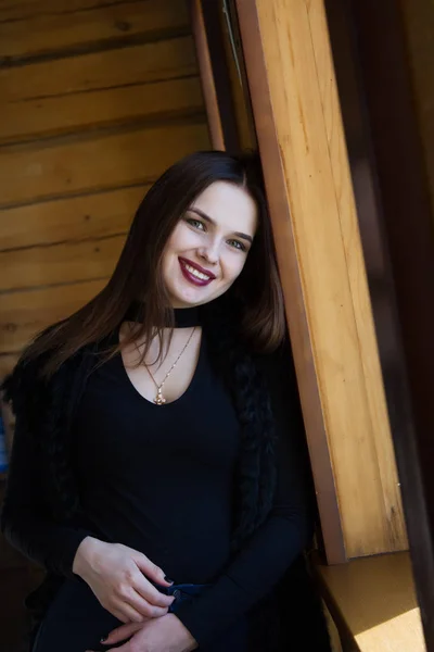 Chica en una cabaña de madera se encuentra junto a la ventana — Foto de Stock