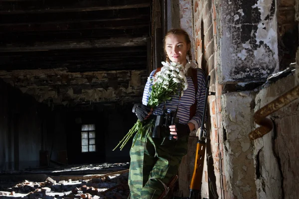 Sniper girl se tient dans un bâtiment en ruine avec un bouquet de camomilles Photos De Stock Libres De Droits