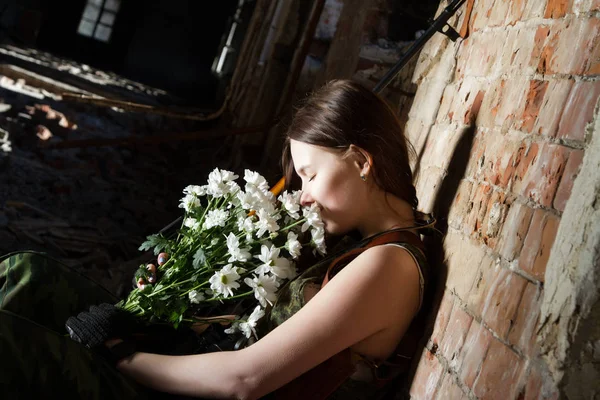 Young sniper girl with flowers and weapons on the background of the ruins — Stock Photo, Image