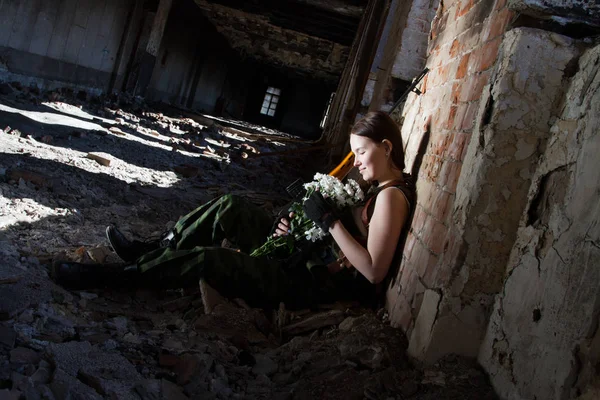 Junges Scharfschützenmädchen mit Blumen und Waffen auf dem Hintergrund der Ruinen — Stockfoto