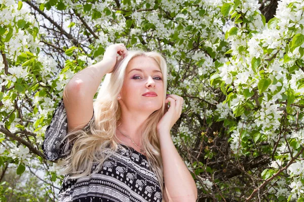 Ung blondin i bakgrunden av blommande äppelträd i trädgården — Stockfoto