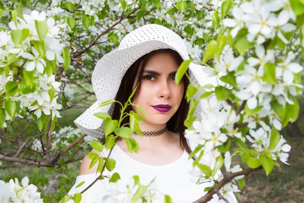 Young girl in a white hat against the background of blooming apple trees in the garden — Stock Photo, Image
