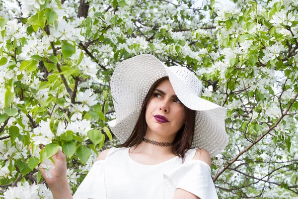 Young girl in a white hat against the background of blooming apple trees in the garden — Stock Photo, Image