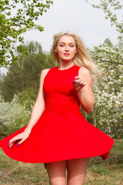 Jong meisje in een korte fladderende jurk tegen de achtergrond van een bloeiende tuin — Stockfoto